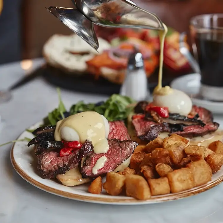 Une assiette avec de bœuf coupé en tranches avec un œuf poché sur le dessus sur lequel on verse de la béchamel chez Maggie Oakes, l’un des meilleurs restaurants familiaux de Montréal.