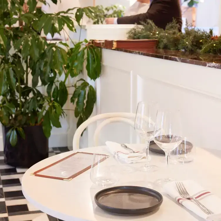 A white restaurant table with glasses of wine and a menu in front of a large green plant from Cocotte Bistro, one of the best brunches in Ottawa.