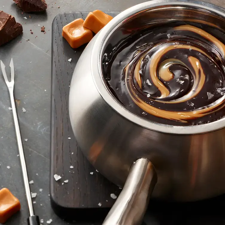 A pot of chocolate and caramel fondue alongside a fondue skewer and pieces of chocolate and caramel from The Melting Pot, one of the best family restaurants in Edmonton.