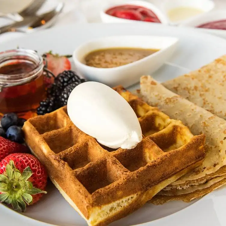 A plate with fruits, a waffle with an egg, crêpes, and maple syrup from Arôme, one of the best brunches in Ottawa.