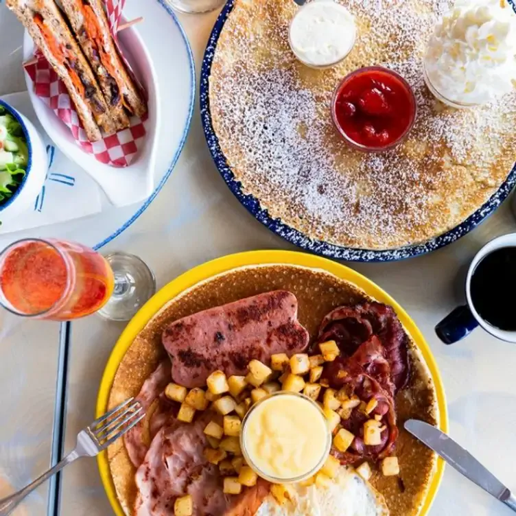 A large pancake with various meats, potatoes, and hollandaise sauce, and a big crêpe with powdered sugar, jam, and whipped cream, accompanied by a cocktail at De Dutch.