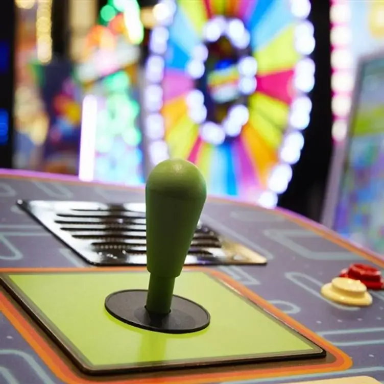 An arcade game controller in front of a colored, illuminated game wheel at The Rec Room, one of the best family restaurants in Edmonton.