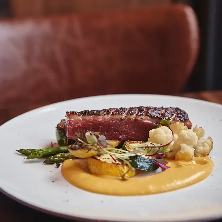 Une assiette avec un morceau de magret de canard accompagné de légumes et d’une sauce jaune chez Maggie Oakes, l’un des meilleurs restaurants familiaux de Montréal.