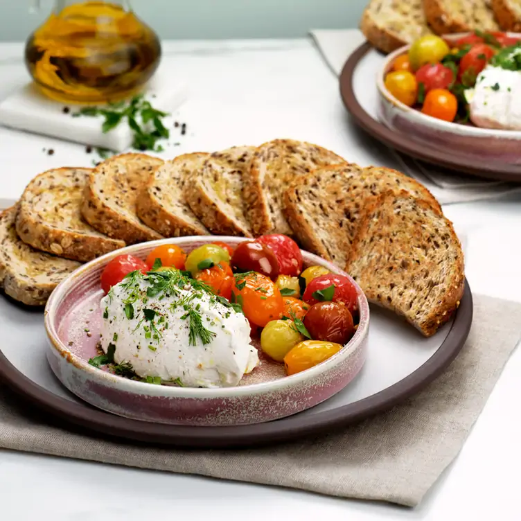 A large plate with grilled tomatoes, slices of grilled bread, and Italian cheese in front of a bottle of olive oil from Moxies, one of the best family restaurants in Edmonton.