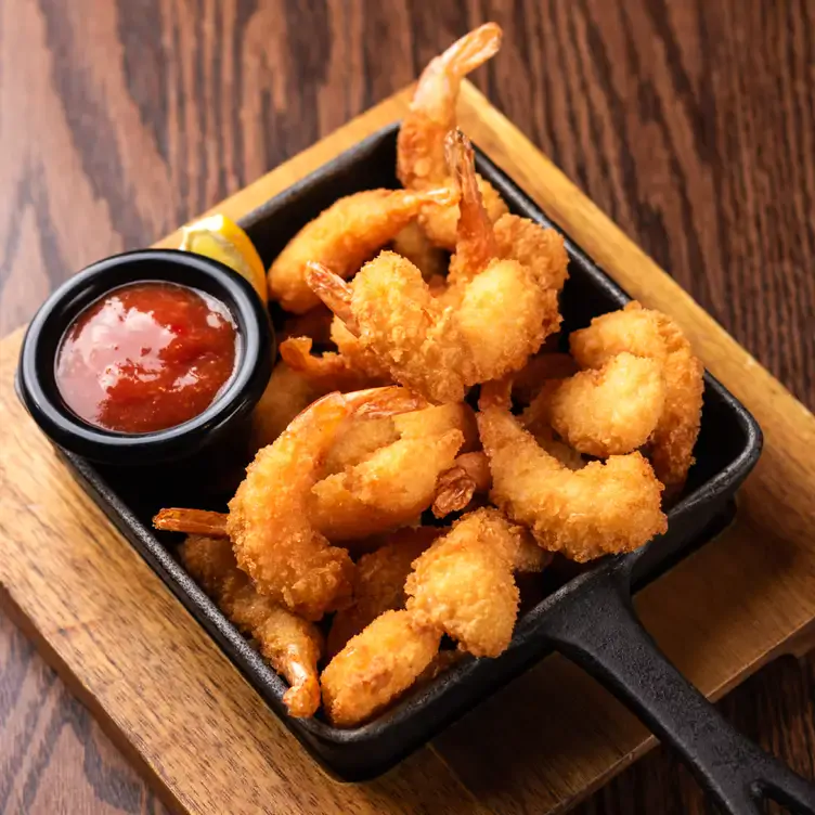 A small skillet containing crispy breaded shrimp and a red dipping sauce from Mr Mikes SteakhouseCasual, one of the best family restaurants in Edmonton.