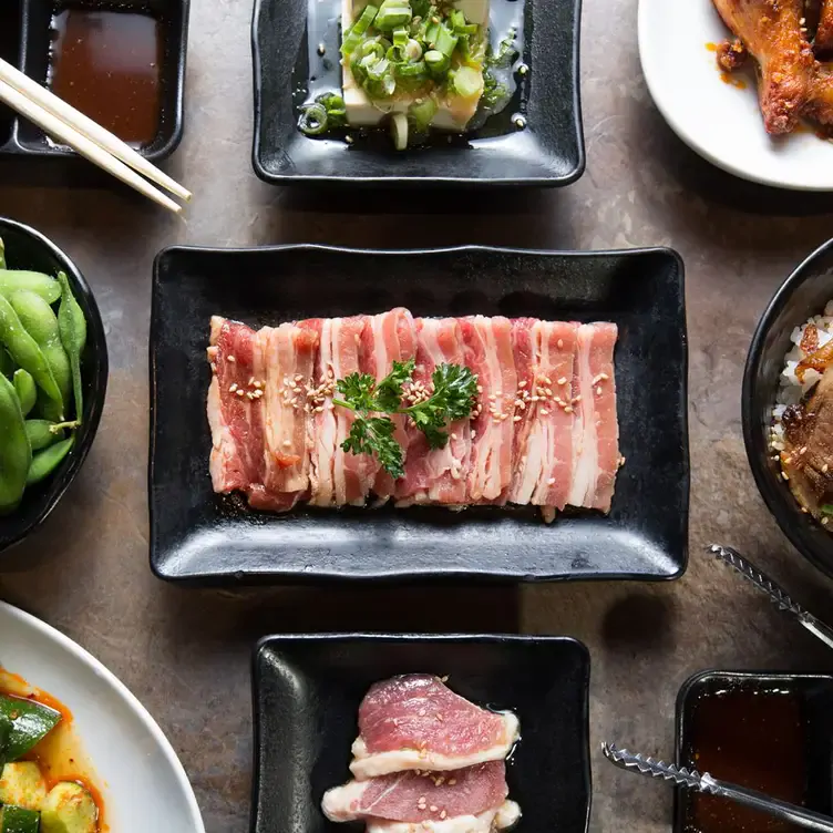 Une assiette de bacon entourée d’autres assiettes avec des viandes, des légumes et du tofu de chez Gyu-Kaku, l’un des meilleurs restaurants familiaux de Montréal.