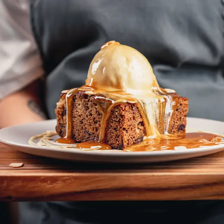 A slice of cake with a scoop of ice cream on top and plenty of caramel sauce drizzled over and around it from Moxies, one of the best family restaurants in Edmonton.