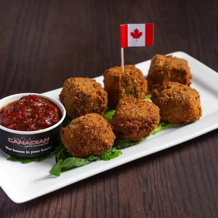 A plate with several small crispy balls placed on a bed of lettuce and accompanied by a dipping sauce from The Canadian Brewhouse, one of the best family restaurants in Edmonton.