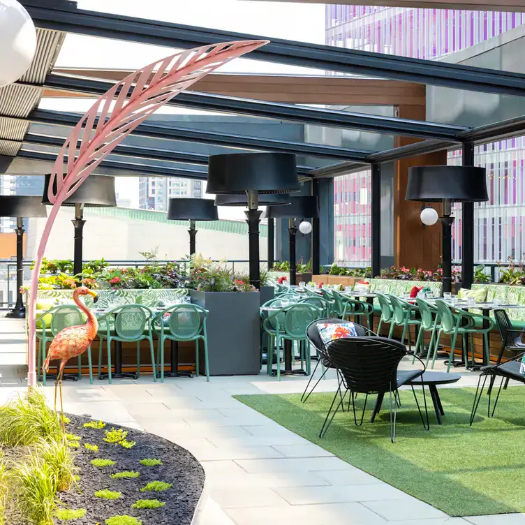 Une terrasse couverte avec de nombreuses tables, des plantes décoratives et un faux flamant rose au Muze Lounge & Terrasse, l’un des meilleurs restaurants sur le toit à Montréal.