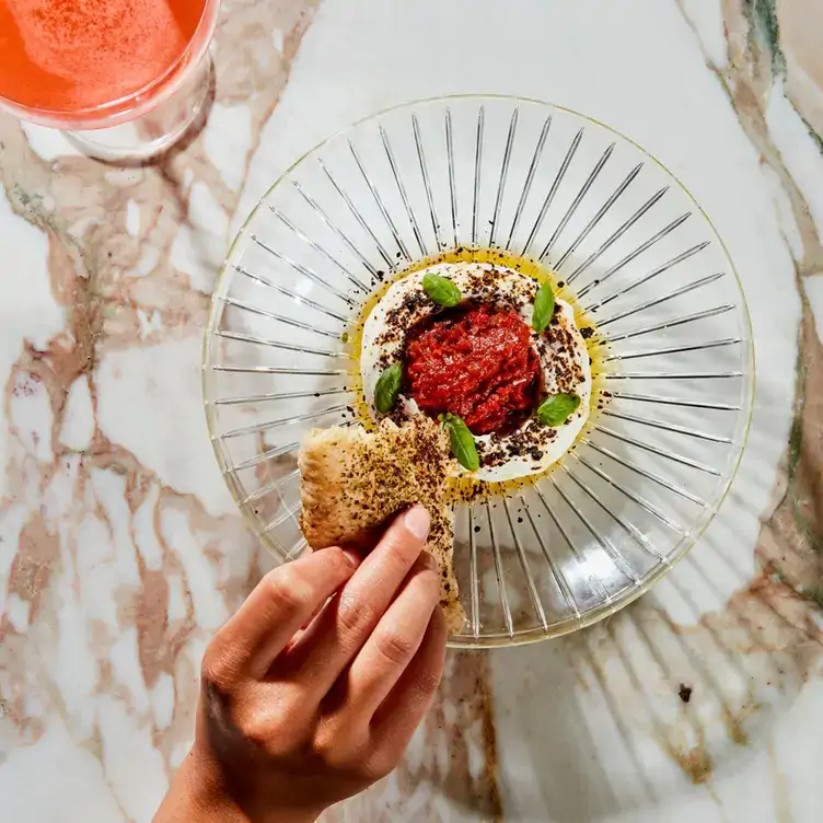 A diner dips bread in a plate of hummus topped with tomato sauce at The Toronto Beach Club