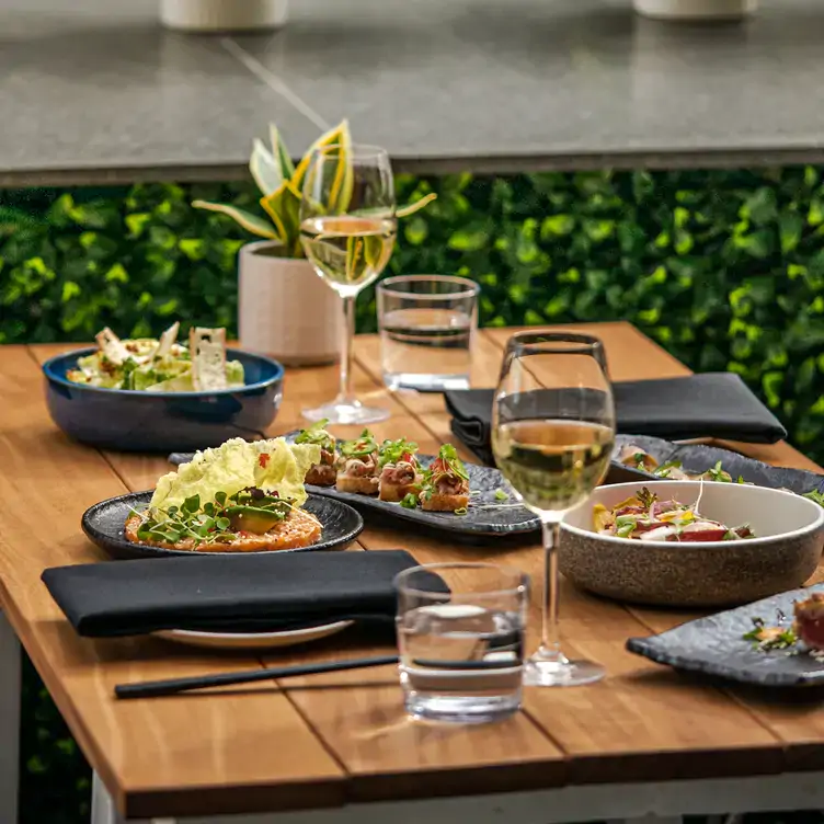 Une table avec plusieurs assiettes de salades et d’entrées accompagnées de deux verres de vin blanc chez Belvu, l’un des meilleurs restaurants sur le toit à Montréal.