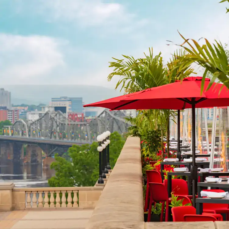 A terrace with red parasols and a background view of the Alexandra Bridge at La Terrasse, one of the best restaurants with a view in Ottawa.