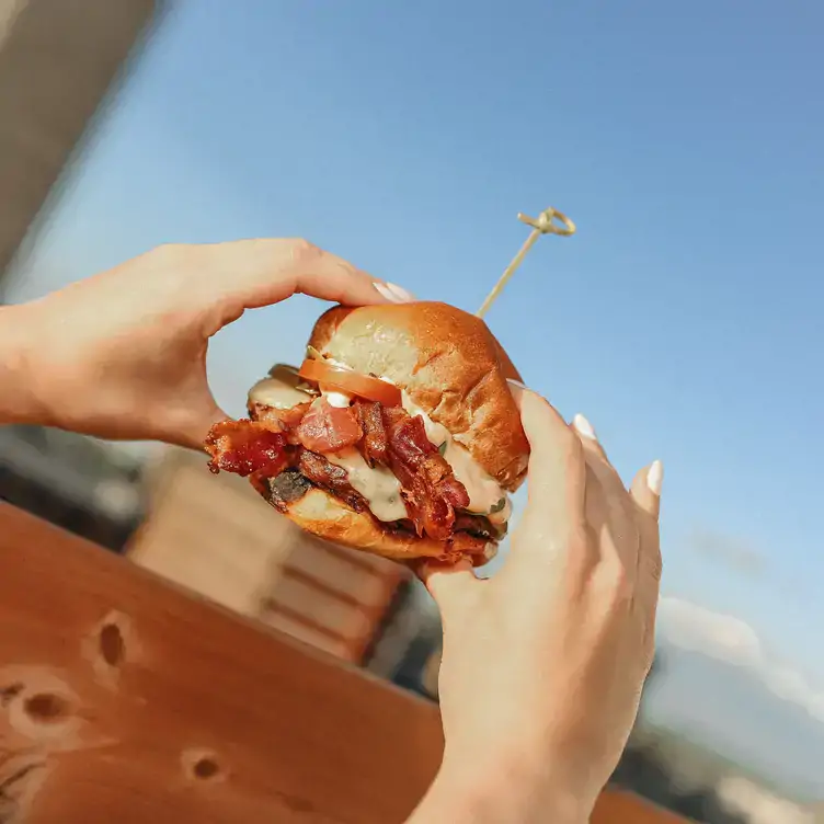 Hands holding a bacon burger from Terrasse Place d’Armes, one of the best rooftop restaurants in Montreal.