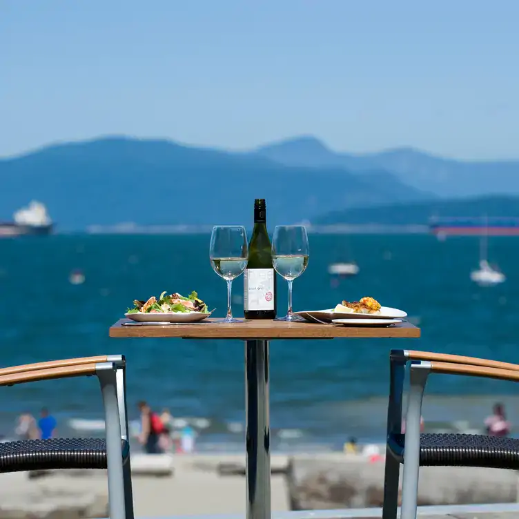 Mountains and ocean behind a table with white wine and salad at The Boathouse at Kits Beach, one of the best view restaurants Vancouver offers.