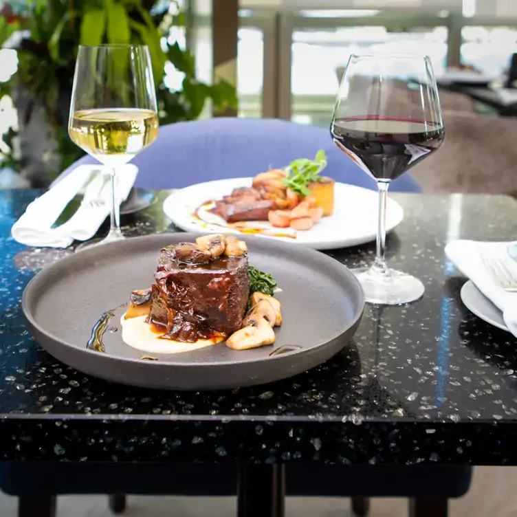 A table with two plates, one containing a piece of beef topped with sauce, accompanied by a glass of red wine and a glass of white wine at Zoe's at Fairmont Chateau Laurier, one of the best restaurants with a view in Ottawa.