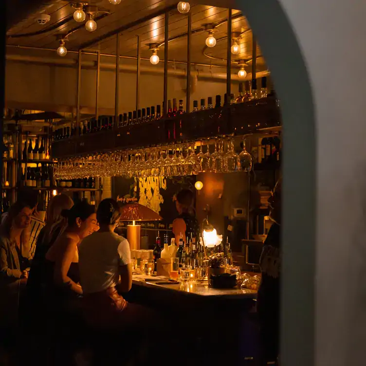 Dimly lit bar area of Frenchie Wine Bar, one of the best bars in Calgary, with wine racks, glasses and people chatting.