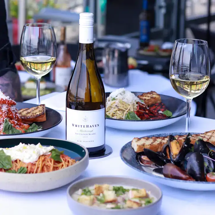 Several plates of different pasta dishes and a plate of mussels around a bottle of white wine from PIER 7 restaurant + bar, one of the best restaurants in North Vancouver.