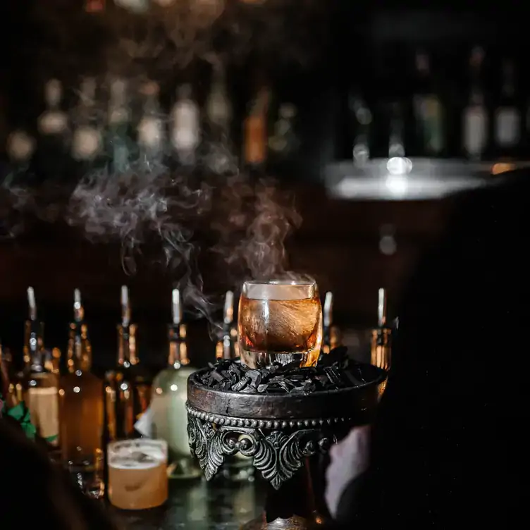 A smoking cocktail on a bar with bottles in the background at BarChef, one of the best bars in Toronto.