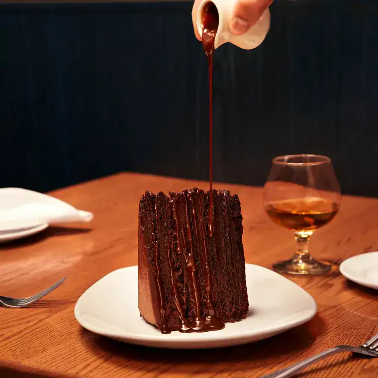 A server pouring chocolate sauce over a slice of chocolate cake at The Keg Steakhouse + Bar, one of Vancouver’s best steakhouses.