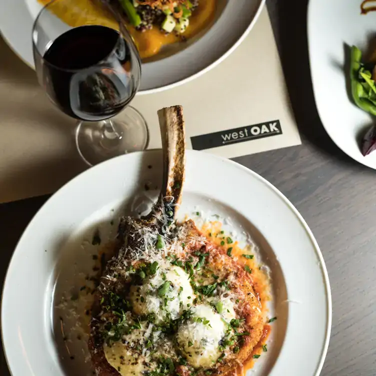 A bone-in Tomahawk steak dressed with butter and a glass of red wine at WestOak Restaurant, the best steakhouse in Vancouver.