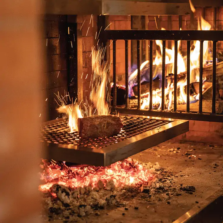 A wood-fired grill showing a log on fire at Bluebird Wood-Fired Steakhouse & Fondue, one of the best steakhouses in Calgary.