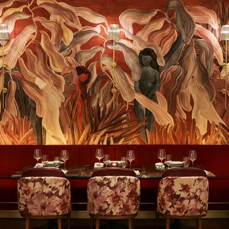 A wall at Frenchy Bar et Brasserie, hand painted in a floral design with red velvet seating and floral chairs shown.