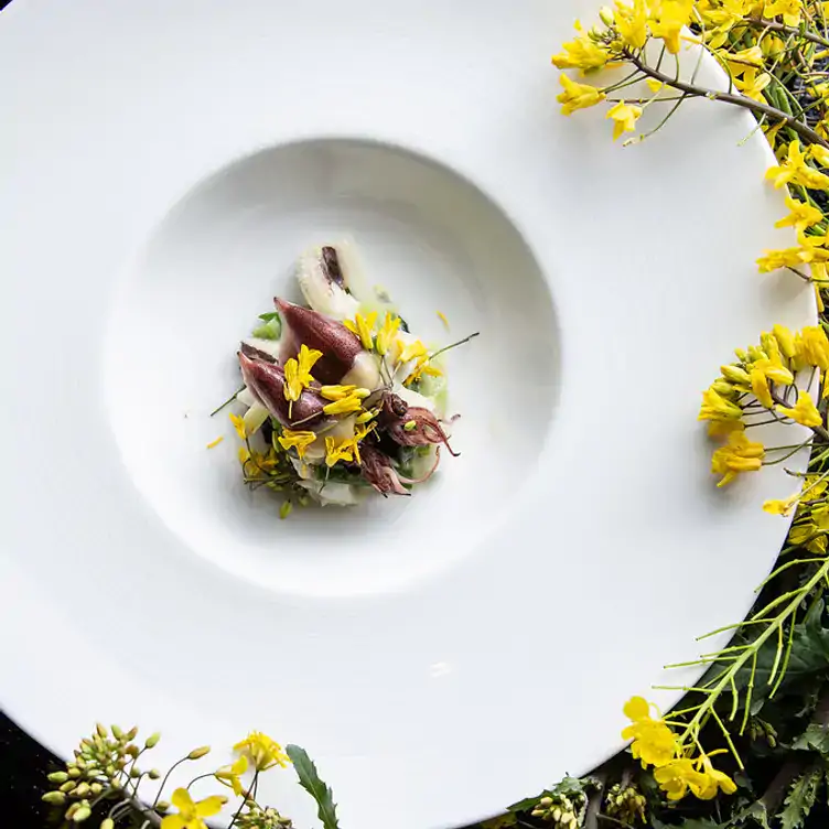 A seafood dish served in a deep white plate, garnished with yellow flowers at Tojo's Restaurant, one of Vancouver’s best fine dining restaurants.