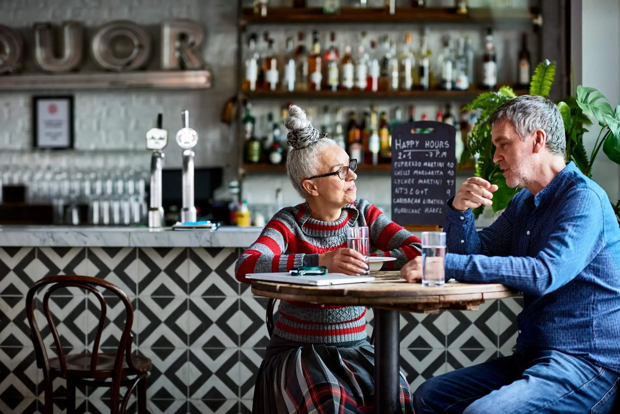 Image depicts two diners seated at a table in a bar.